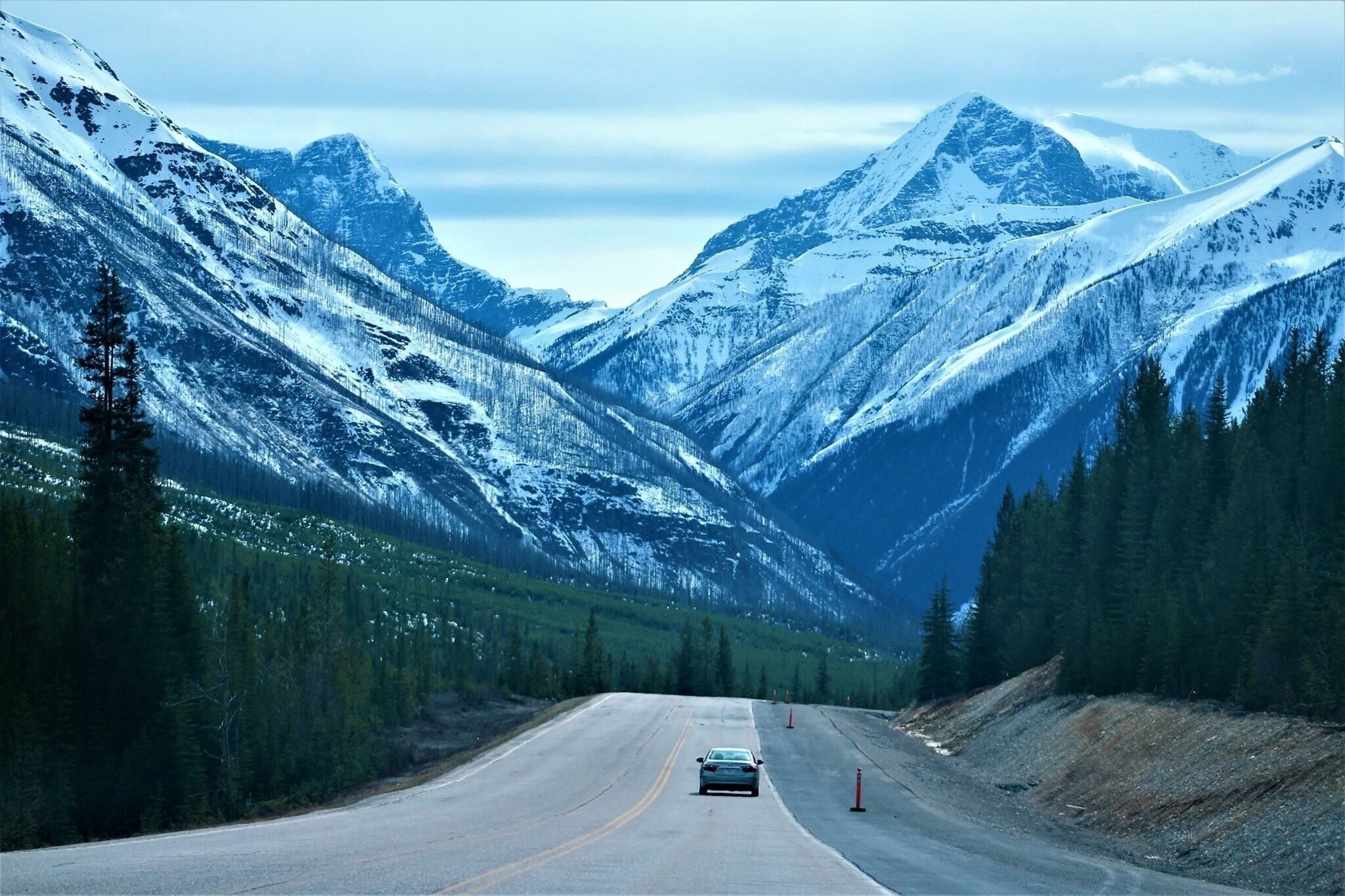 Eine verschneite Bergstraße, auf der ein Auto in Richtung eines Berggipfels fährt.