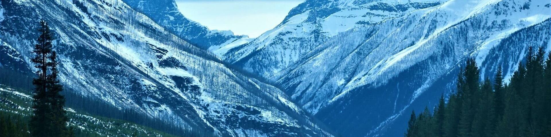 A snow-covered mountain road with a car driving towards a peak.