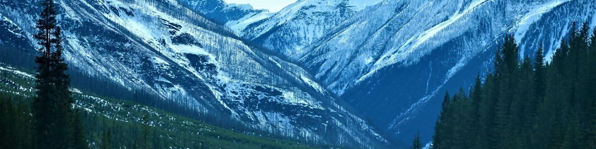 Estrada montanhosa coberta de neve, com um carro seguindo em direção ao cume.