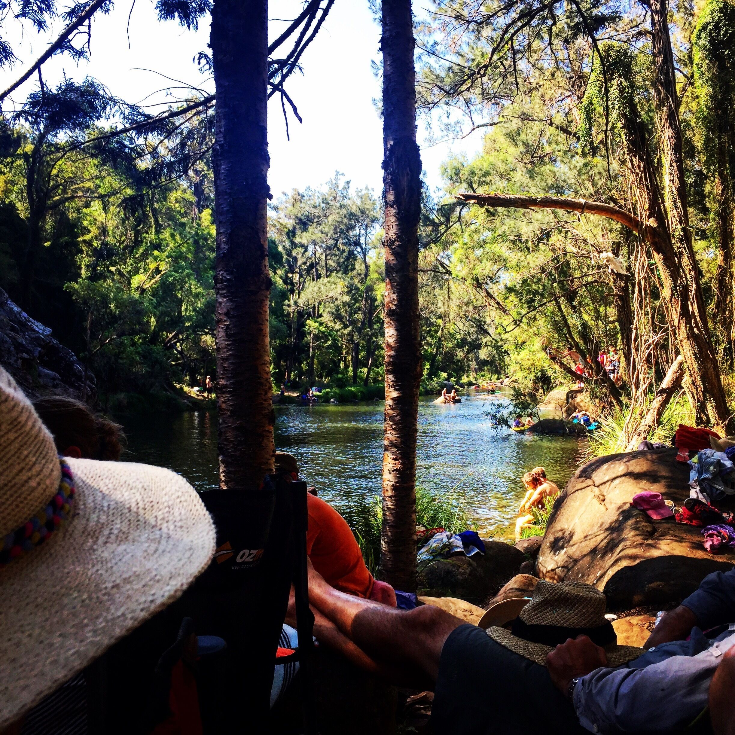 A river surrounded by trees with people sitting and standing on rocks.