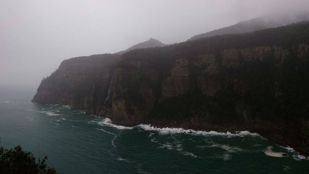 A coastal cliff with a waterfall and ocean waves crashing against it.