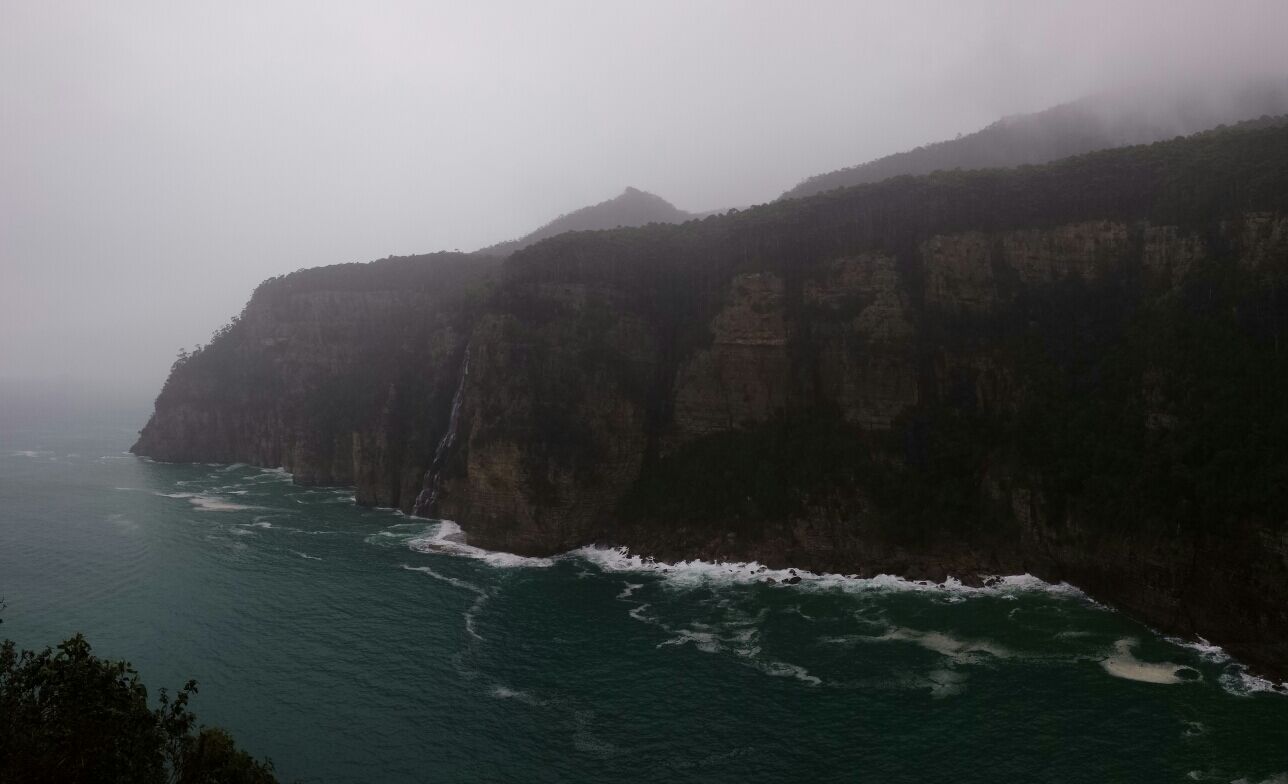 A coastal cliff with a waterfall and ocean waves crashing against it.