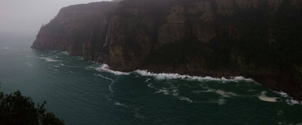 A coastal cliff with a waterfall and ocean waves crashing against it.