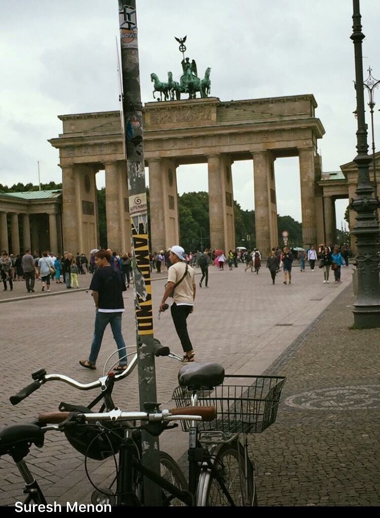 A large historical monument with columns, a statue on top, and people walking around.