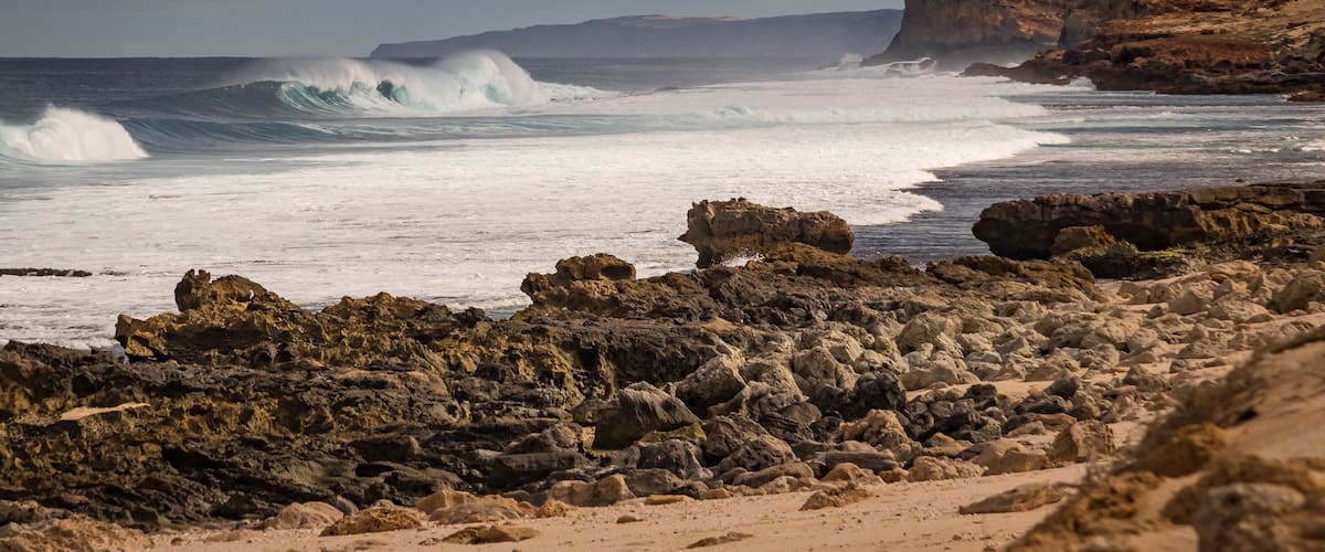 A rocky coastline with waves crashing against the shore and cliffs in the background.