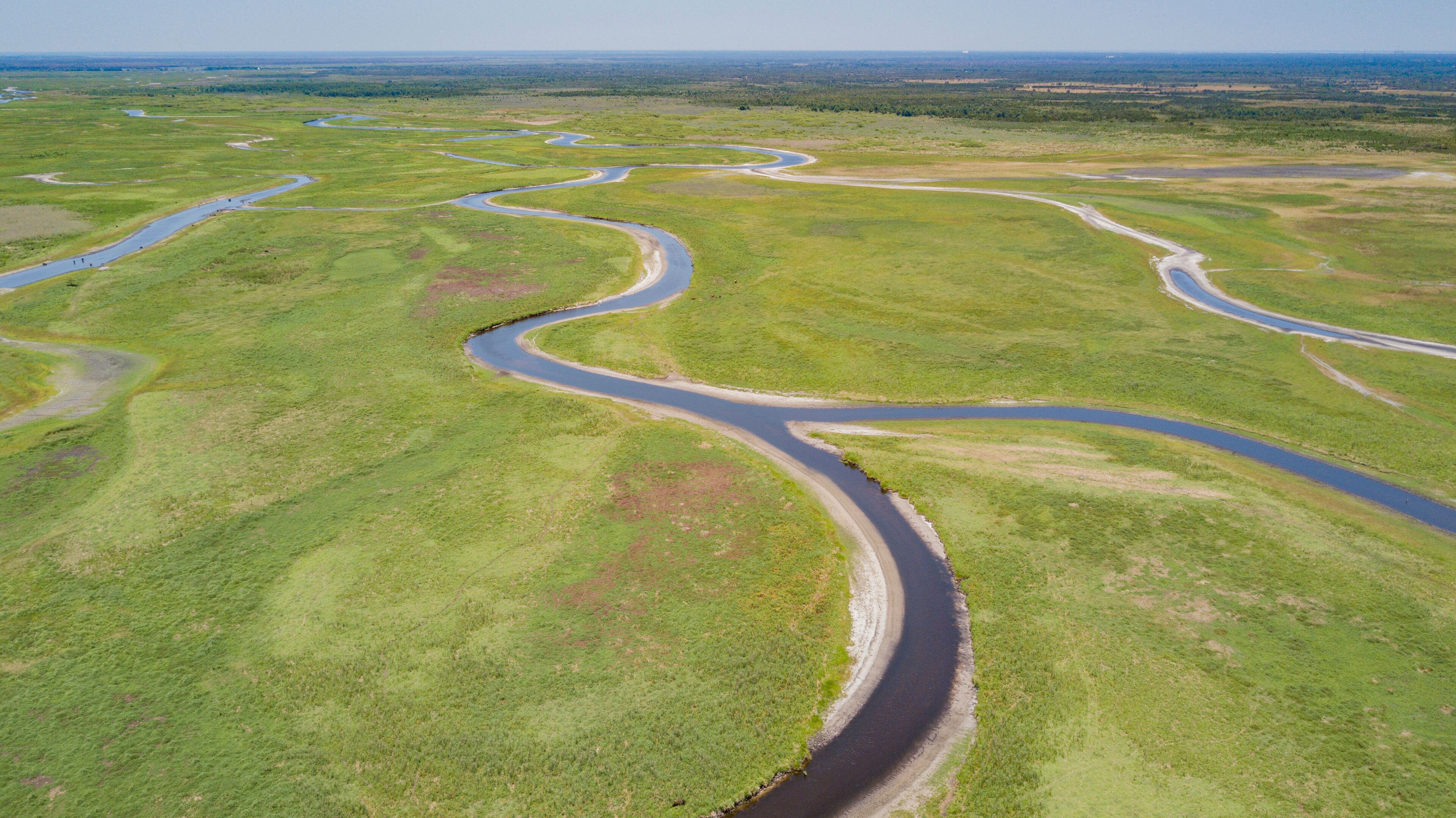 A winding river through a green landscape with multiple bends and a clear sky.