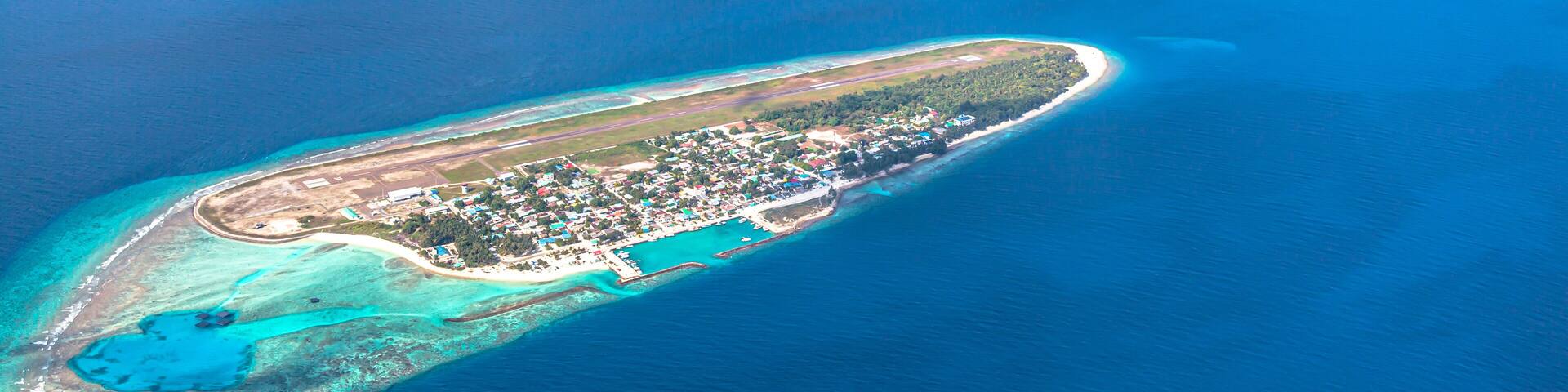 An aerial view of a chain of turquoise atolls with a developed island at the end.
