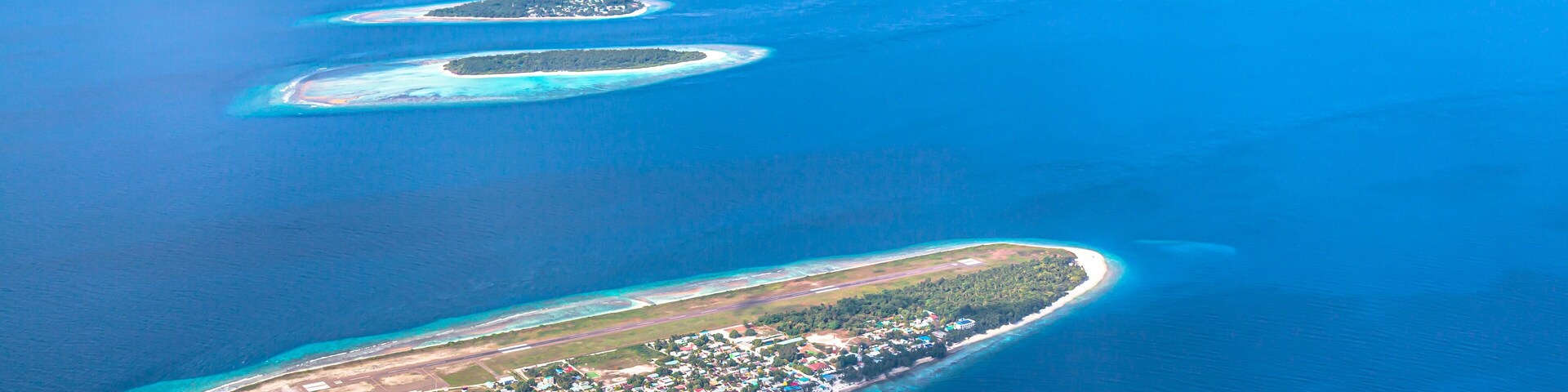Vista aérea de una cadena de atolones turquesa, con una isla desarrollada al final.