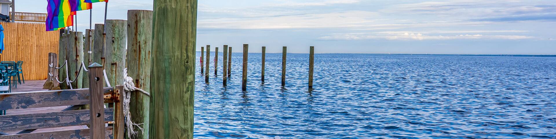Pride flags in a dock with sea view and blue sky in Fire Island, New York.