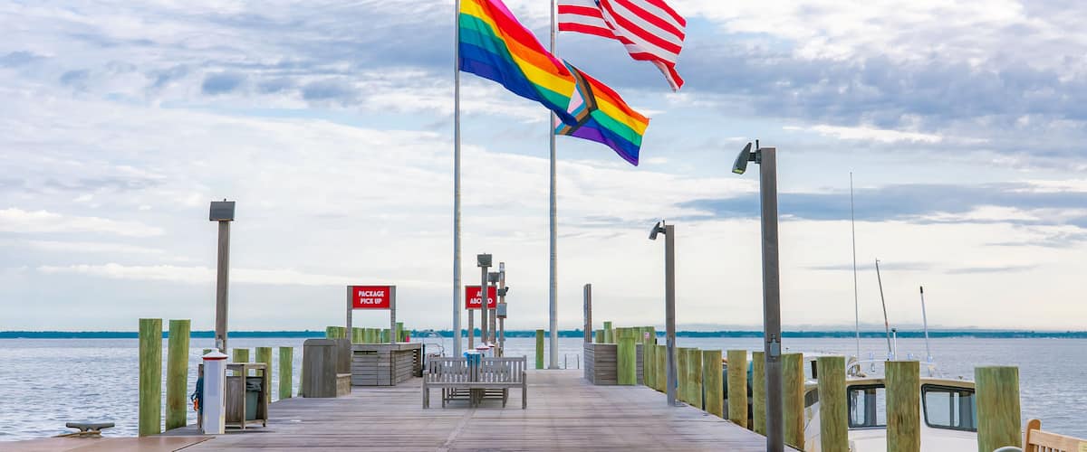 Eine Mole mit Regenbogenflagge und US-amerikanische Flagge, Holzpfosten und einer Bank.