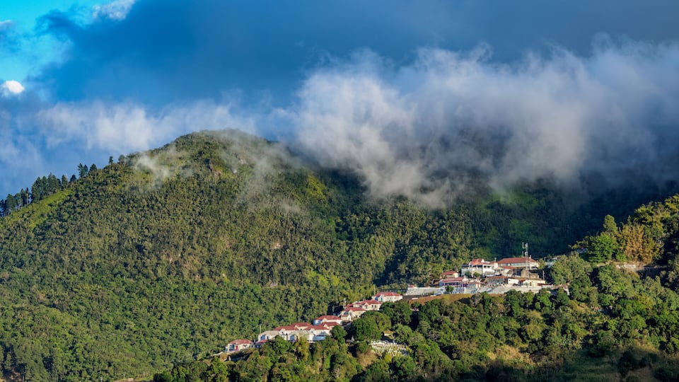 A hillside village with houses nestled among dense forests and mountains.