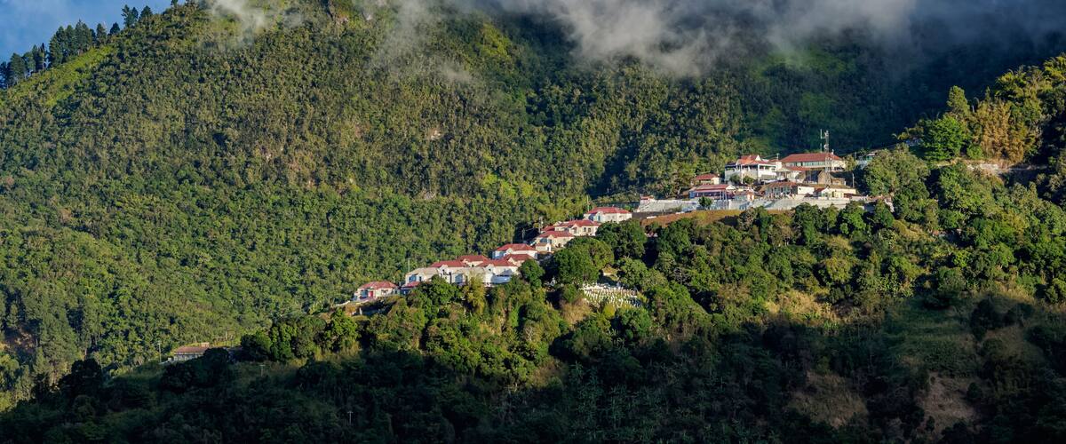 A hillside village with houses nestled among dense forests and mountains.
