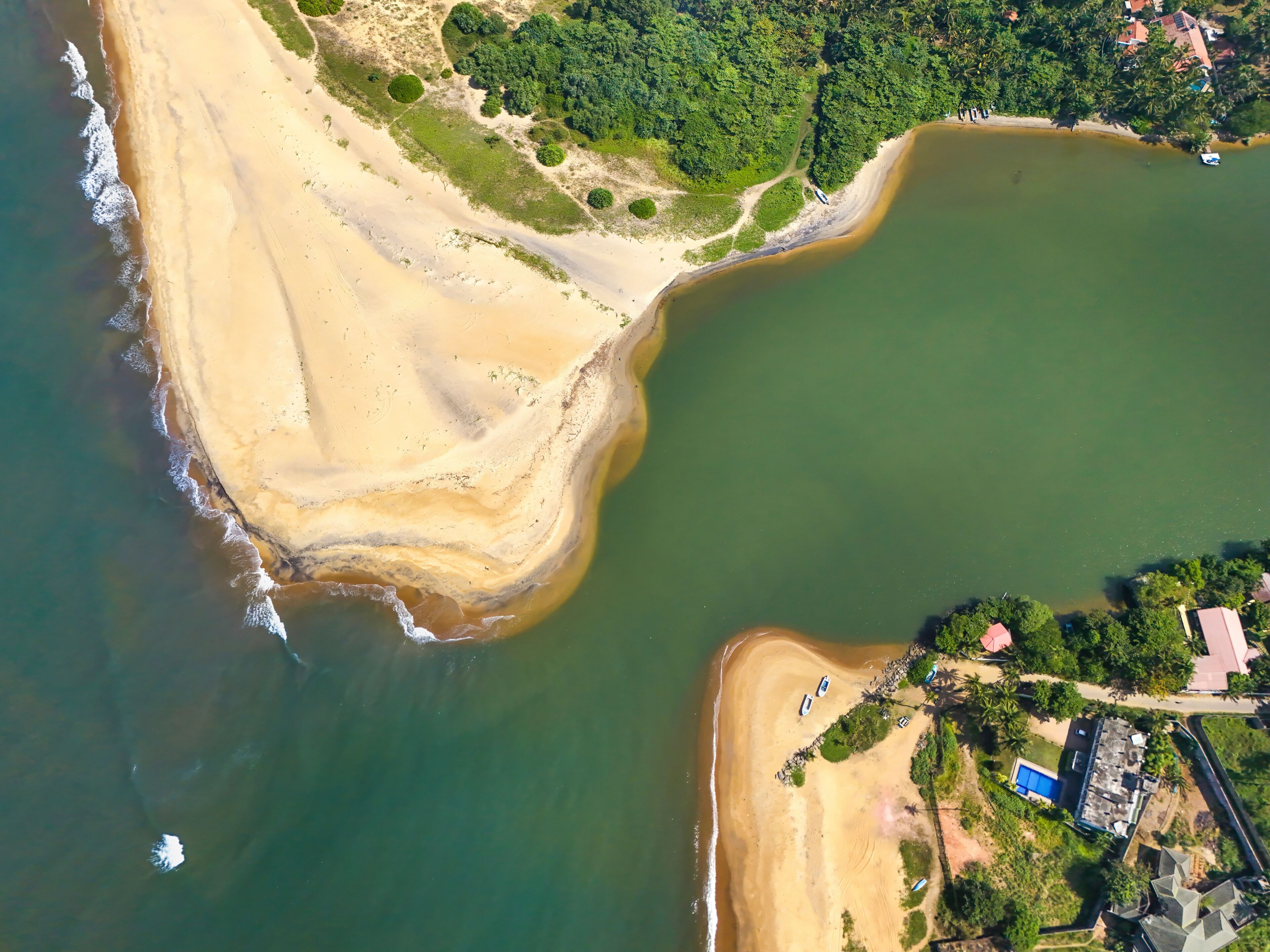 An aerial view of a coastal area with a sandy beach, a green forested area, and a body of water.