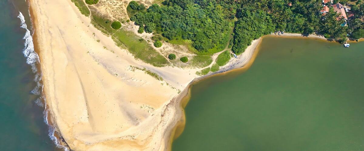 An aerial view of a coastal area with a sandy beach, a green forested area, and a body of water.