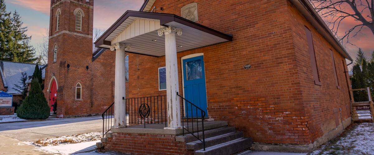 A brick church with a bell tower, a blue door, and a snow-covered ground.