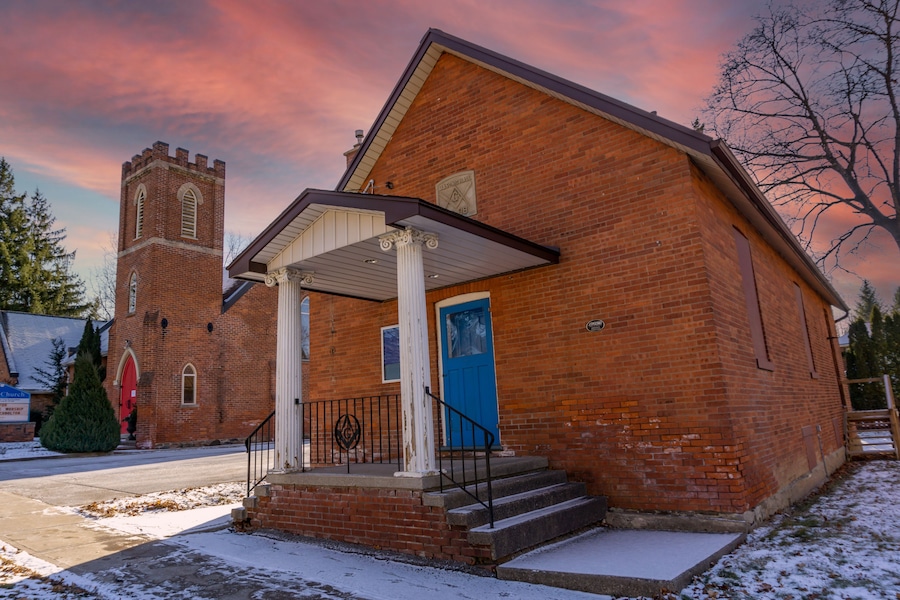 Una iglesia de ladrillo con un campanario, una puerta azul y un suelo cubierto de nieve.