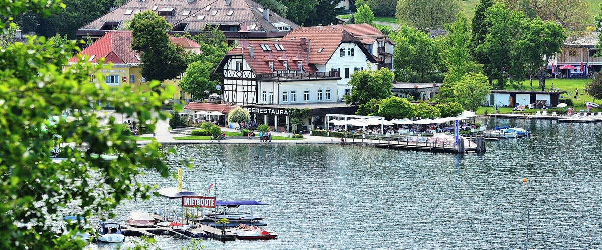 A lakeside town with historic buildings, a pier, and boats.