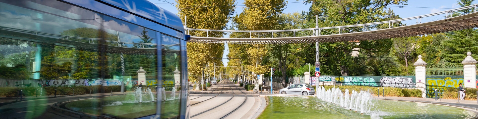 Un autobus bleu, une fontaine, des arbres et un pont.
