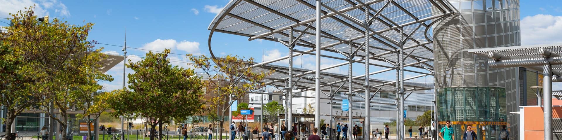 A modern public square with a large metal canopy, a fountain, and people walking.
