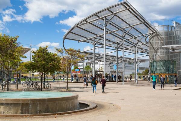 A modern public square with a large metal canopy, a fountain, and people walking.