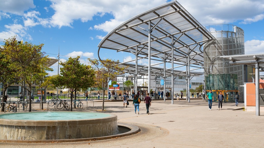 A modern public square with a large metal canopy, a fountain, and people walking.