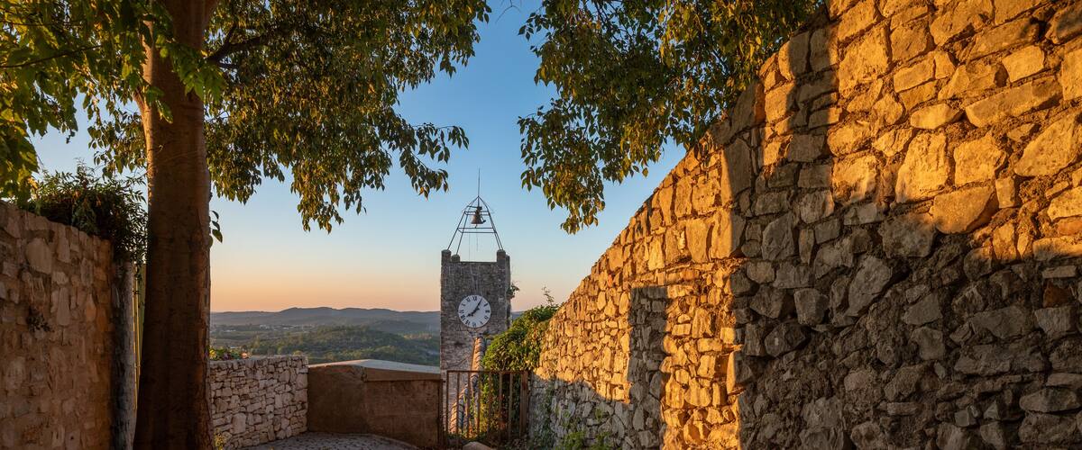 A cobblestone path leading to a stone wall with a clock tower in the background.