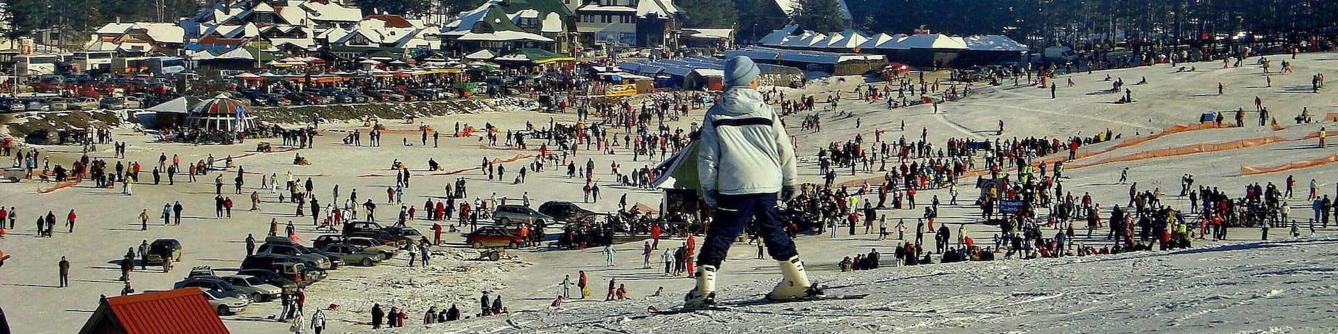 A snowy ski resort with a large crowd, ski lifts, and buildings in the background.