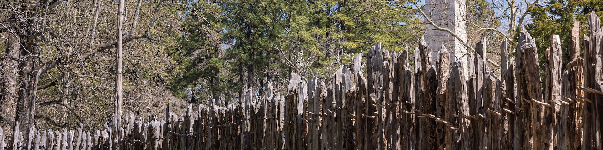 Jamestowne, VA, USA - April 1, 2013: Historic site. Tencentennial obelisk monument seen over defense wall of fort against blue sky. Some green foliage and British flag.