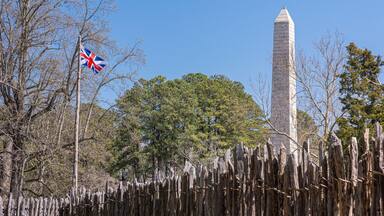 Jamestowne, VA, USA - April 1, 2013: Historic site. Tencentennial obelisk monument seen over defense wall of fort against blue sky. Some green foliage and British flag.