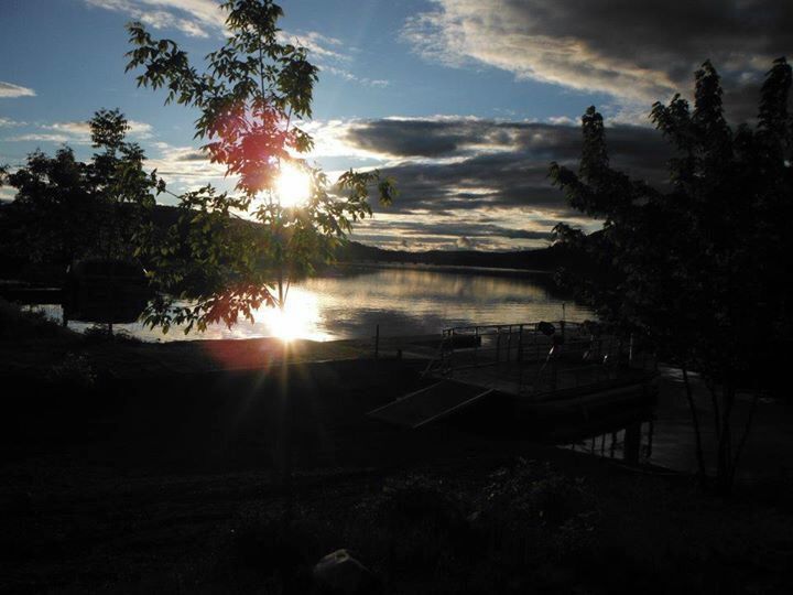 A sunset over a lake with a dock and trees.