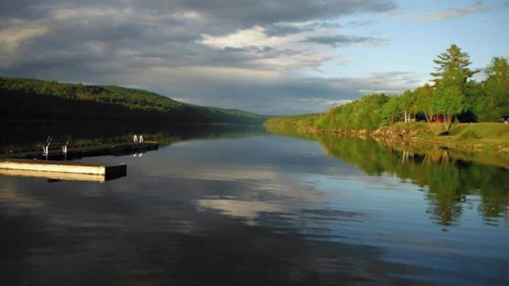 A calm lake with a dock, surrounded by trees and hills.