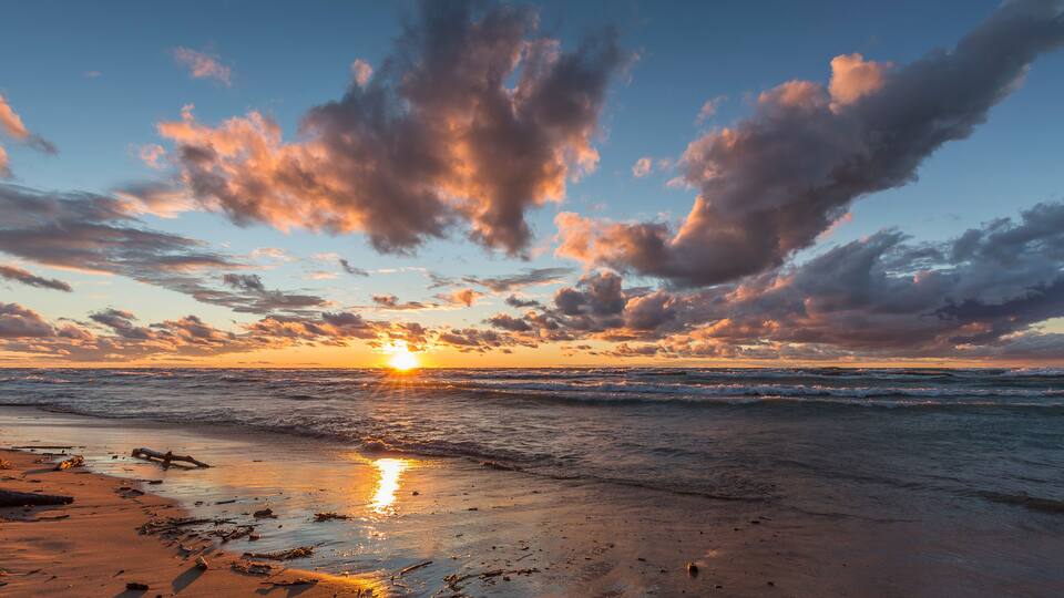 A sunset over a beach with scattered driftwood and waves.