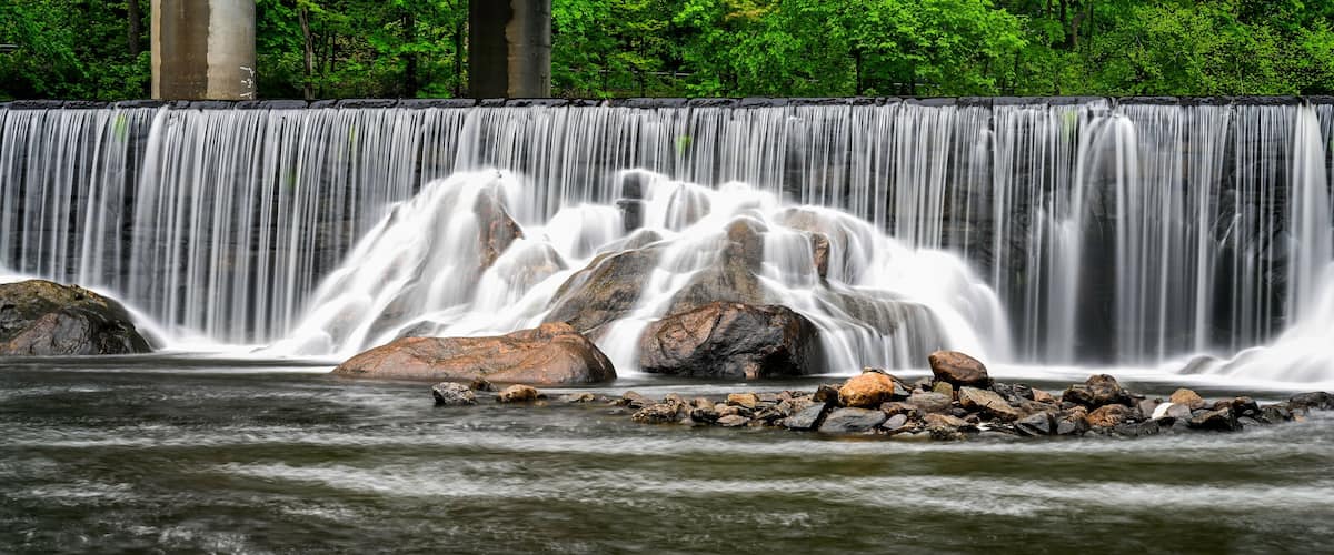 A waterfall cascading over rocks into a river, surrounded by lush green trees.