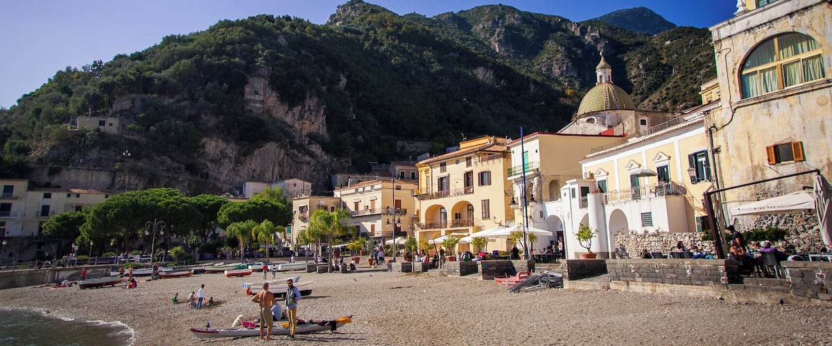 Un pueblo costero con edificios, una playa y montañas al fondo.