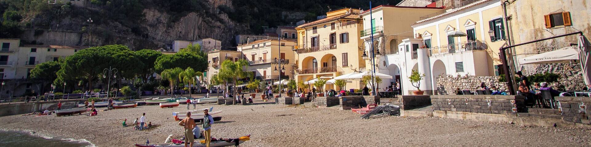 A coastal town with buildings, a beach, and mountains in the background.