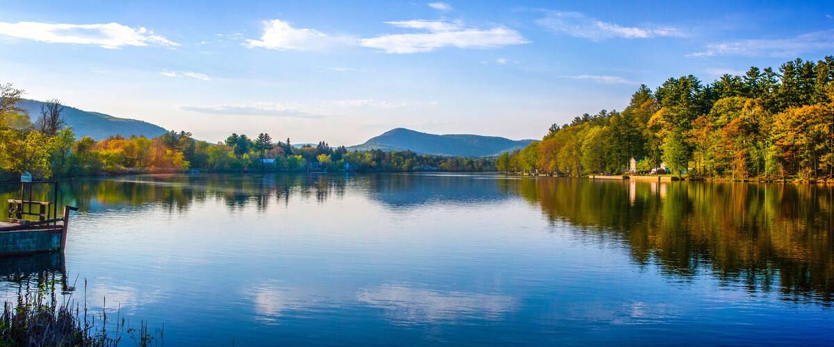 A calm lake surrounded by autumn-colored trees and distant mountains.