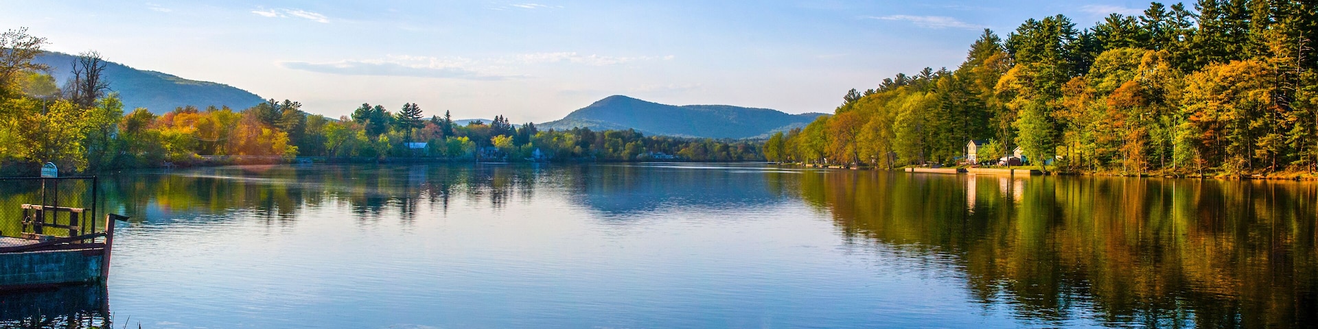 A calm lake surrounded by autumn-colored trees and distant mountains.