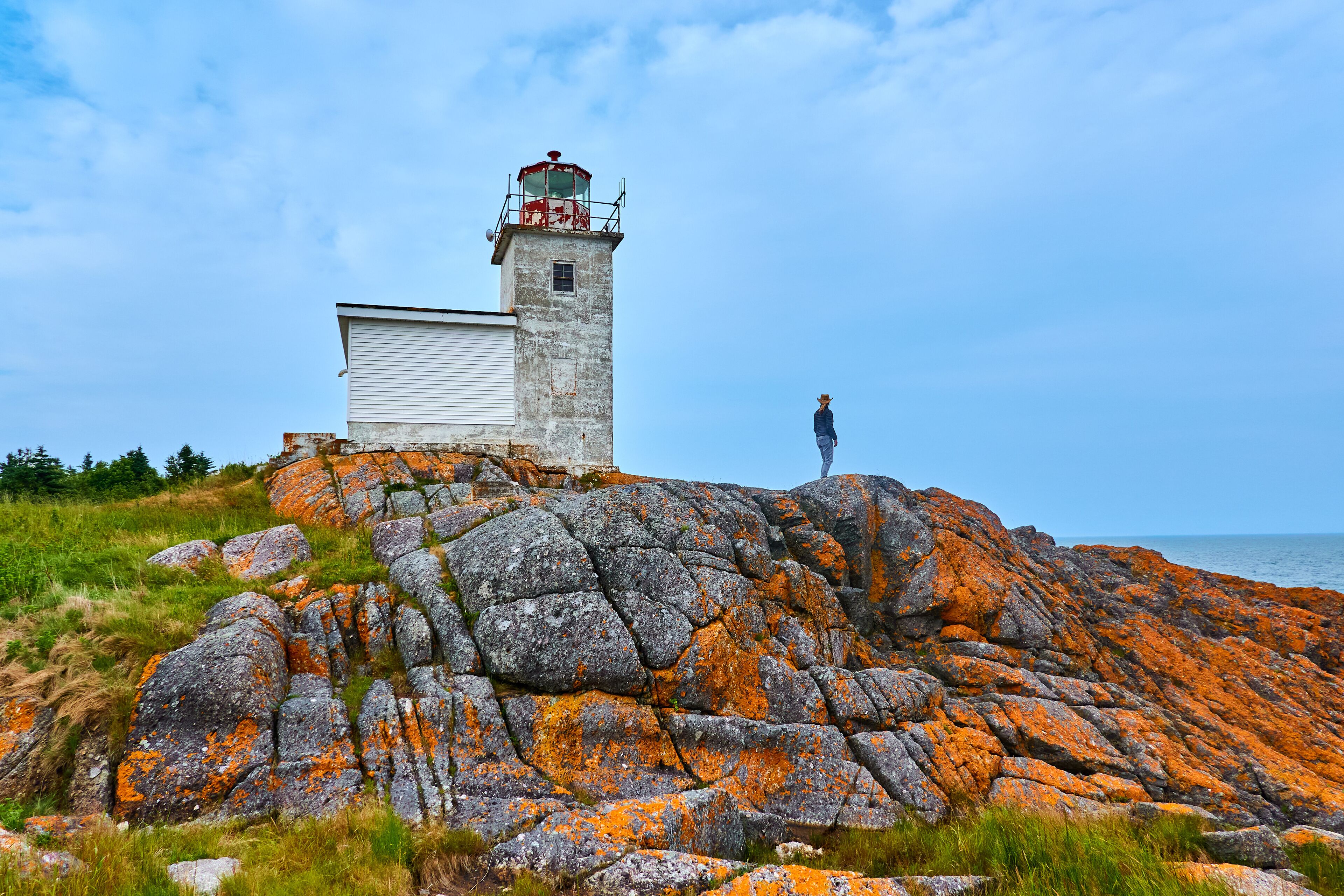 A lighthouse on a rocky outcrop with a person standing nearby.