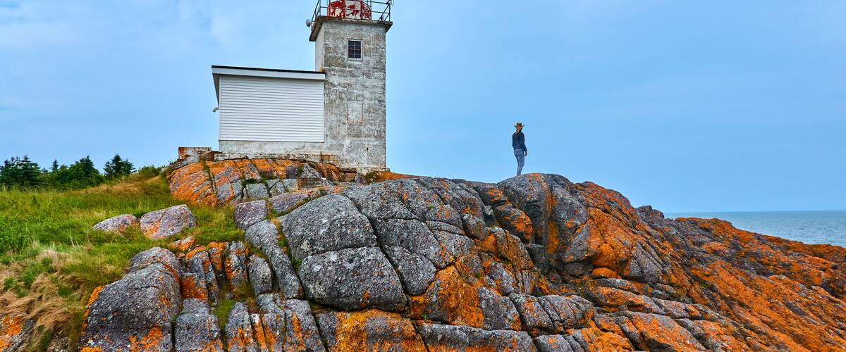 A lighthouse on a rocky outcrop with a person standing nearby.