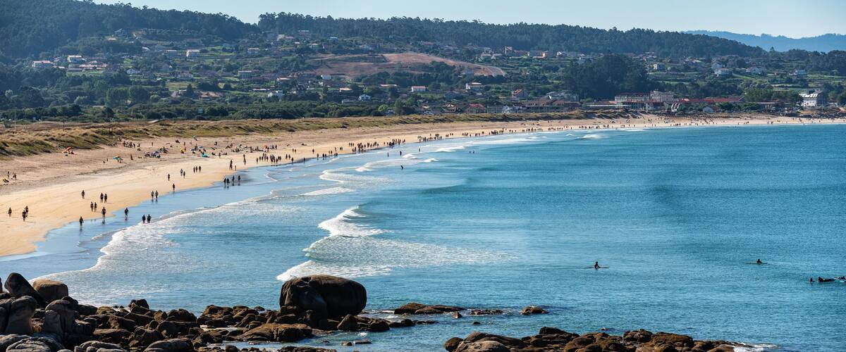 A coastal beach with people, waves, and a town in the background.