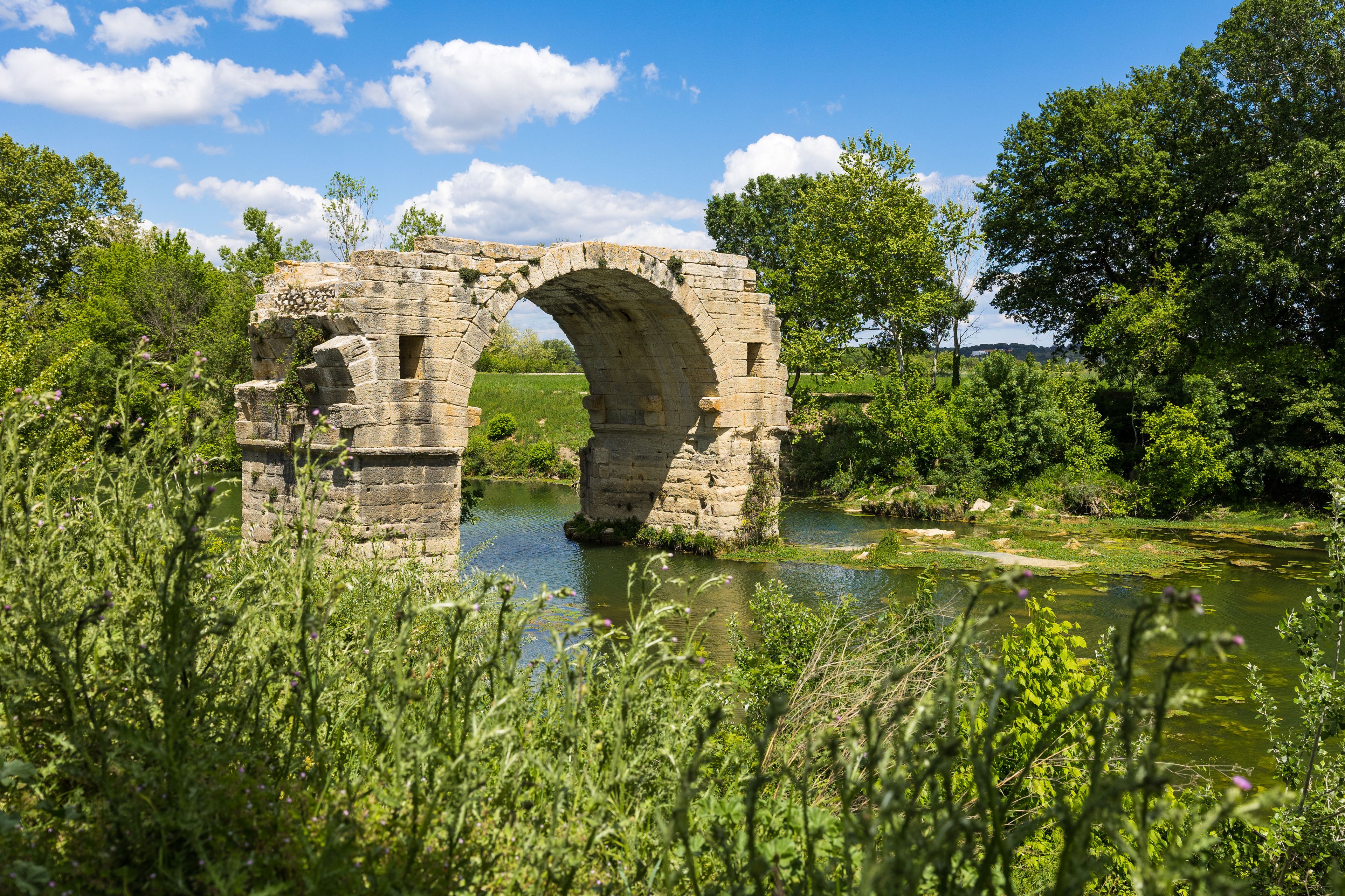 An ancient stone bridge over a river, surrounded by lush greenery and trees.