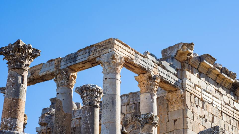 Ancient stone columns and a partially intact structure against a clear blue sky.
