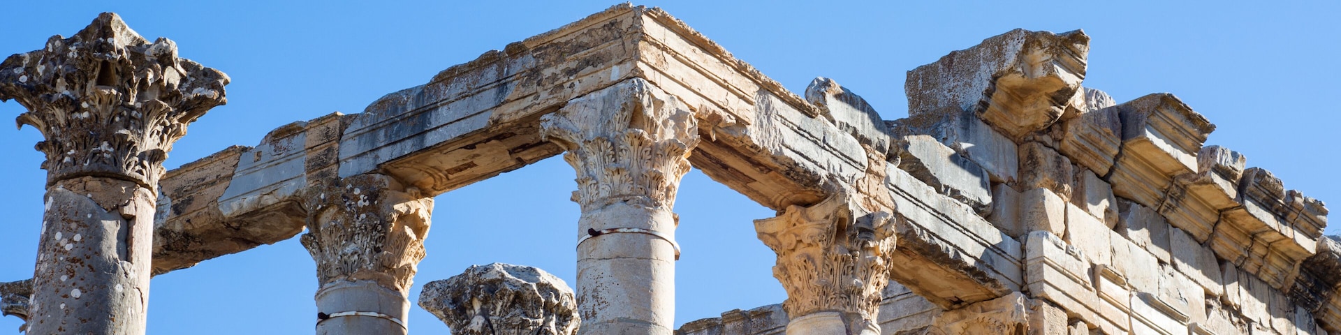 Ancient stone columns and a partially intact structure against a clear blue sky.