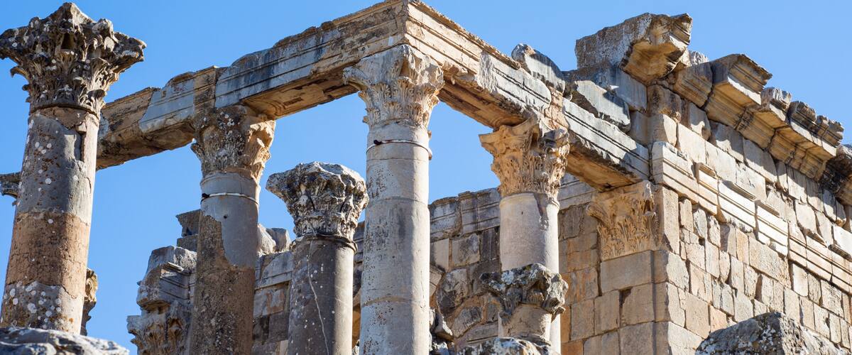Ancient stone columns and a partially intact structure against a clear blue sky.