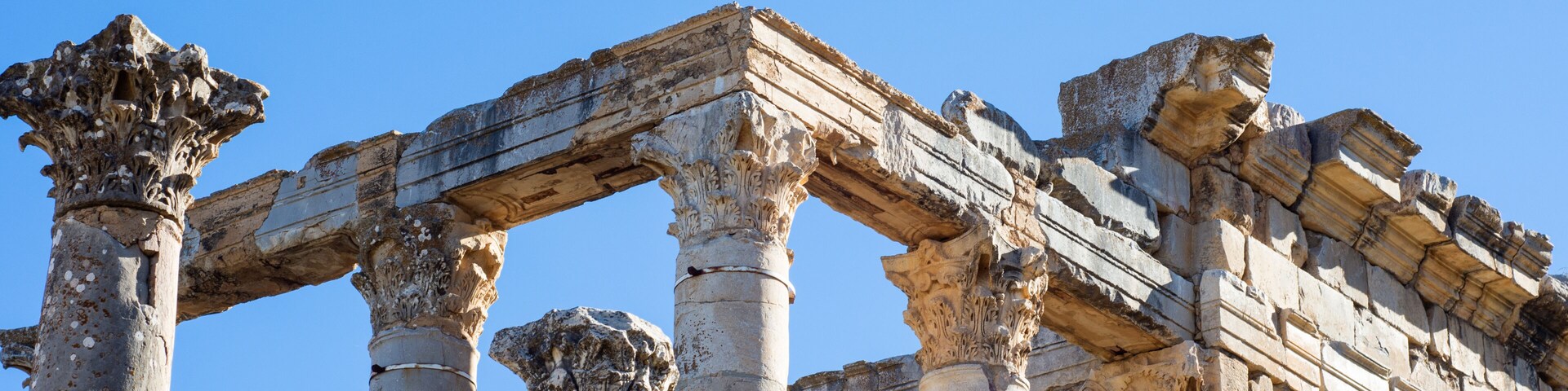 Ancient stone columns and a partially intact structure against a clear blue sky.