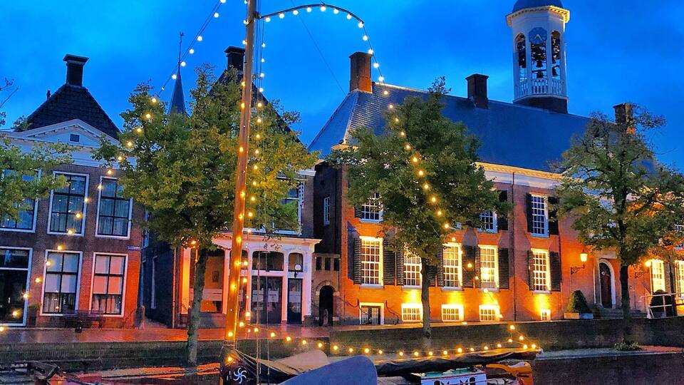 A historic building with a tower, a boat docked by the water, and string lights.
