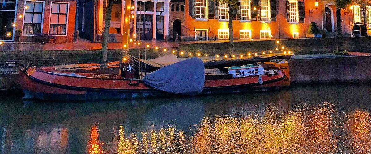 A historic building with a tower, a boat docked by the water, and string lights.