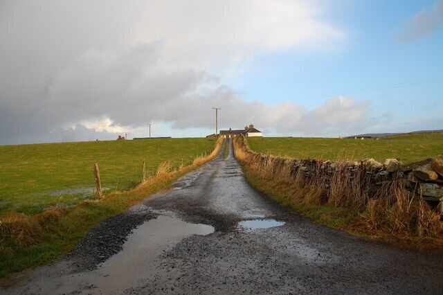 A rural road with puddles, stone walls, and a distant building.
