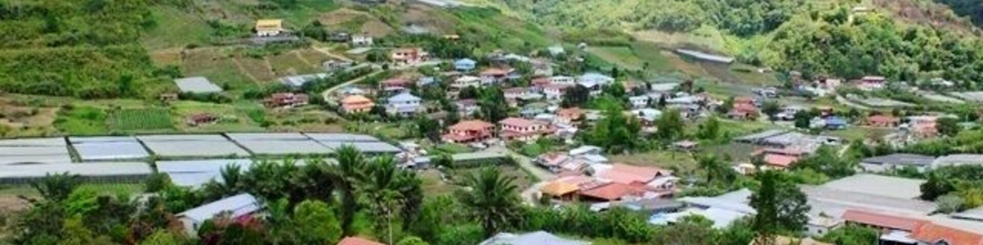 Uma aldeia numa encosta, com casas, campos em socalcos e montanhas ao fundo.