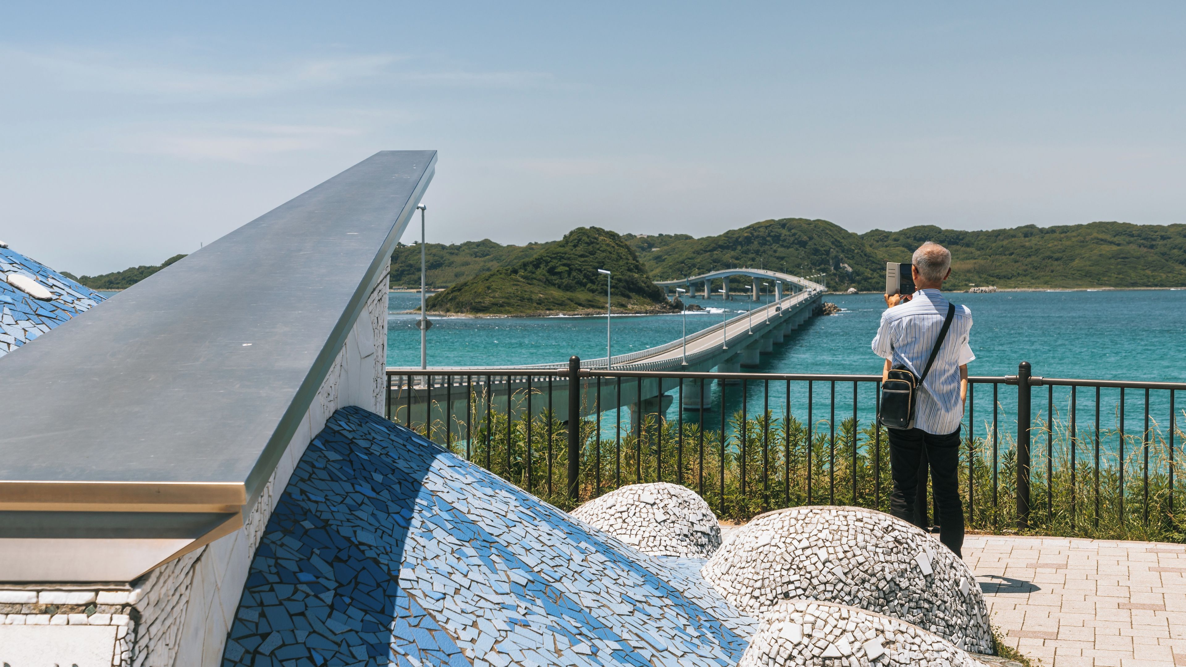 A coastal bridge, a tiled structure, and a person taking a photo.